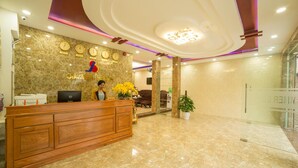 A hotel reception area with a marble reception desk, a clock, and a potted plant. - Summer Beach (Da Nang)