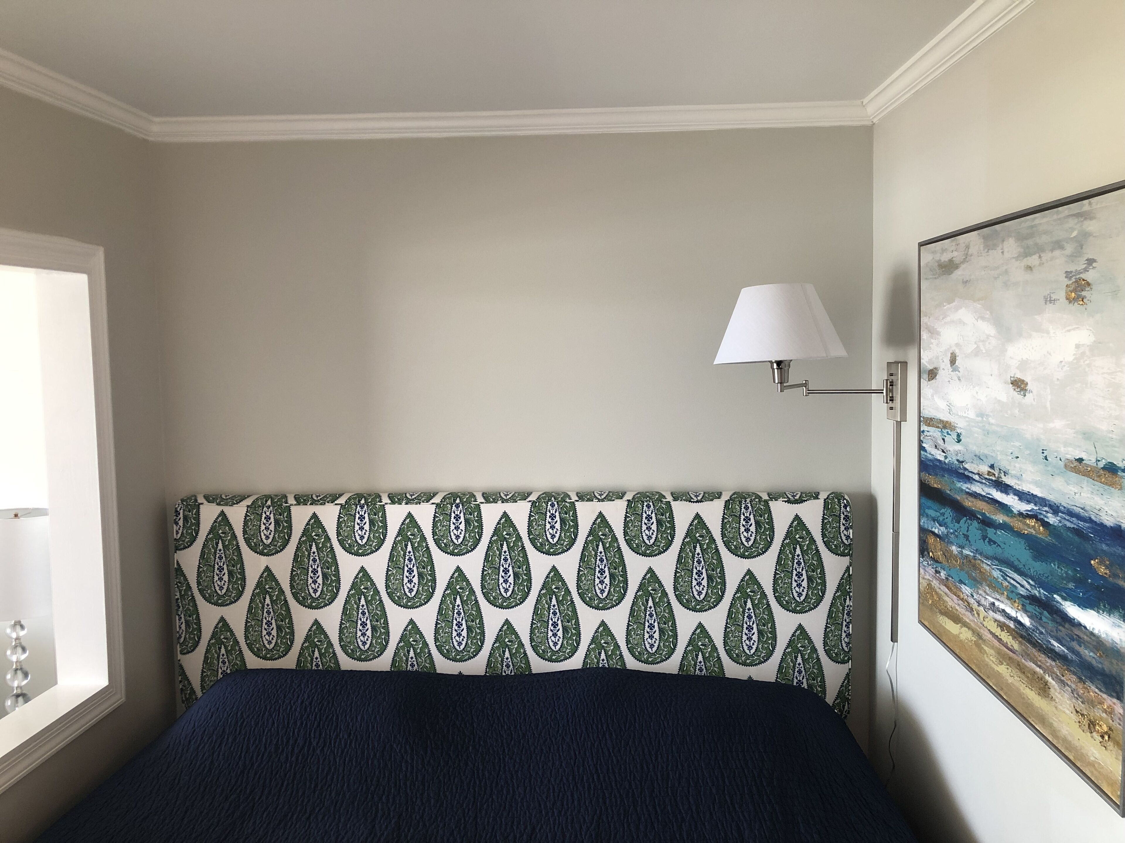 A bedroom with a patterned headboard, a bedside lamp, and a painting on the wall.