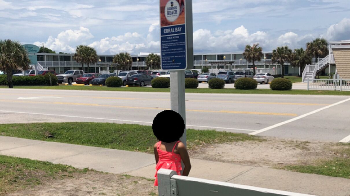 A parking lot with a sign for Atlantic Beach, Coral Bay, and a building in the background.