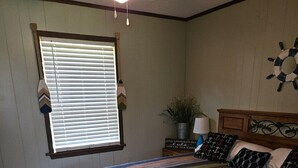 Une chambre à coucher avec un lit en bois, une literie à rayures, une fenêtre avec des stores, une plante et une horloge murale.
