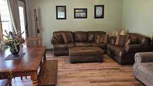 Un salon avec une table à manger en bois, des canapés en cuir marron et un ventilateur de plafond.