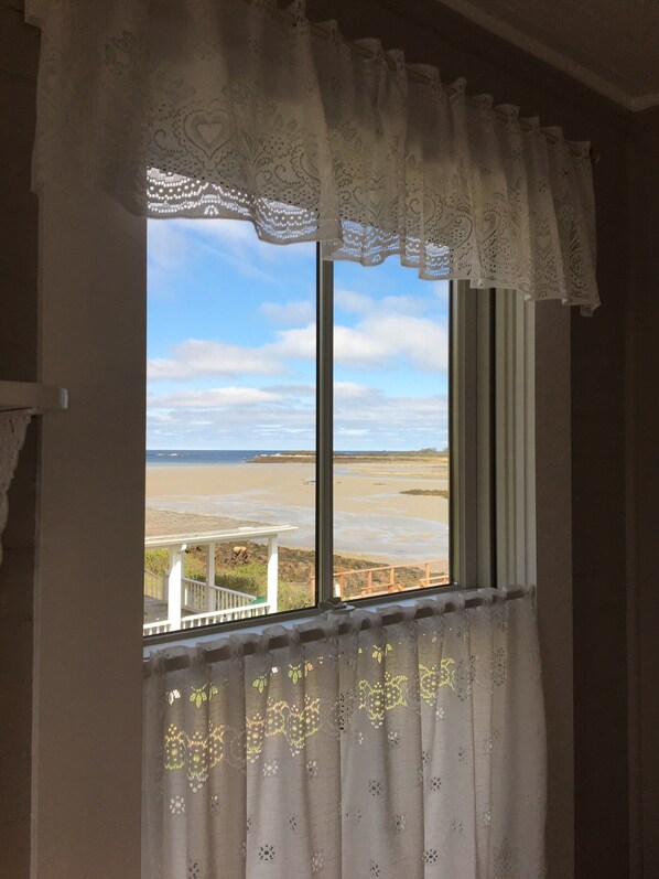 Una ventana con vista a la playa, cortinas y una barandilla blanca.