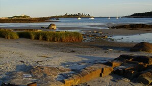 A beach with boats, rocky terrain, and grassy areas.