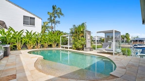 Ein Pool mit gewölbter Kante, umgeben von einer Terrasse mit Liegestühlen und einem Glasgazebo.