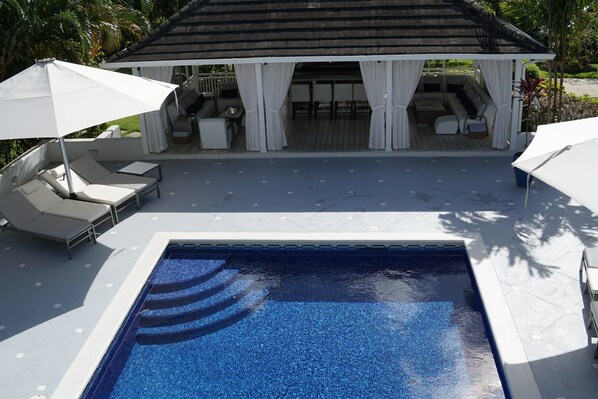 A pool area with lounge chairs and umbrellas, a covered seating area, and a wooden deck.