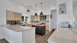A modern kitchen with a large island, pendant lighting, and a clock on the wall.
