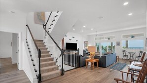 A spacious living area with a staircase, a flat-screen TV, a sofa, and a dining area with chairs and tables.