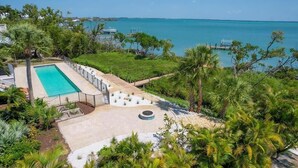 A pool with a view of the ocean, surrounded by greenery and a clear sky.