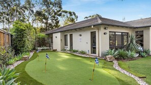 A residential property with a well-maintained lawn, a small garden area with plants, and a house with a tiled roof and large windows.