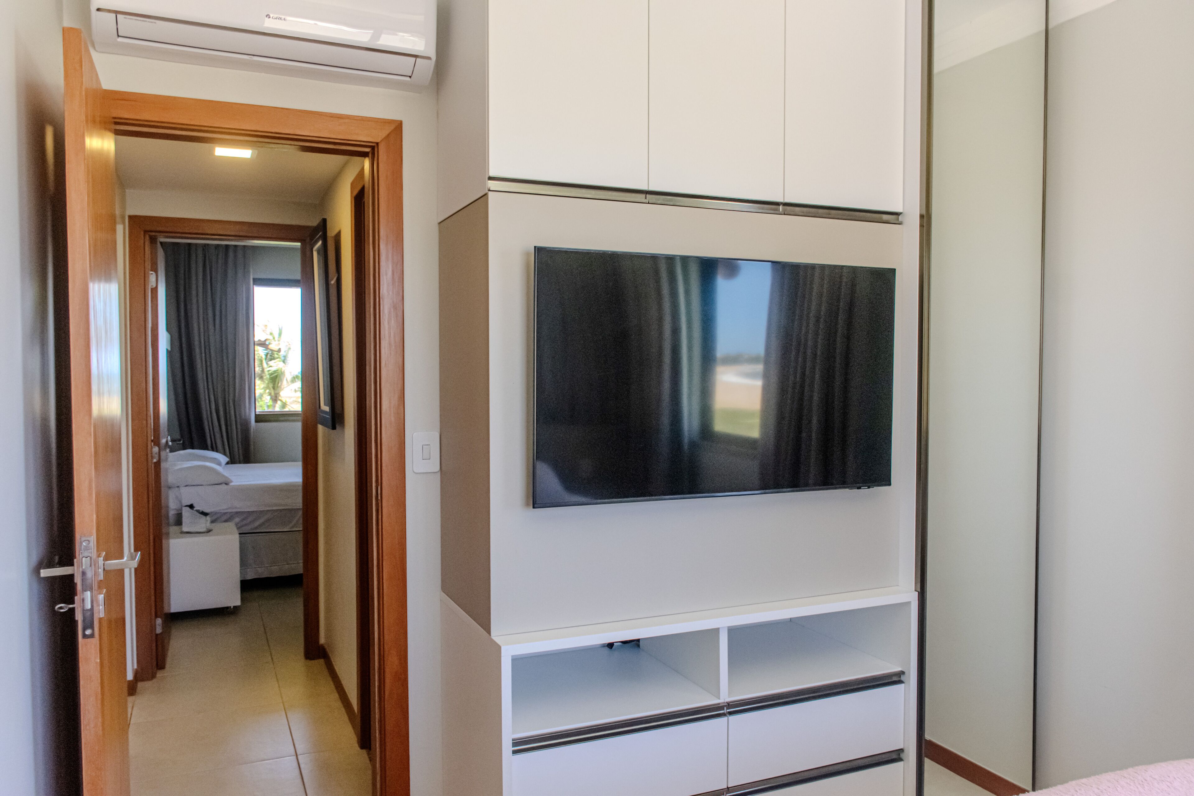 Habitación de hotel con un televisor de pantalla plana grande montado en la pared, una cama con cabecera blanca y un vestidor con puertas correderas.