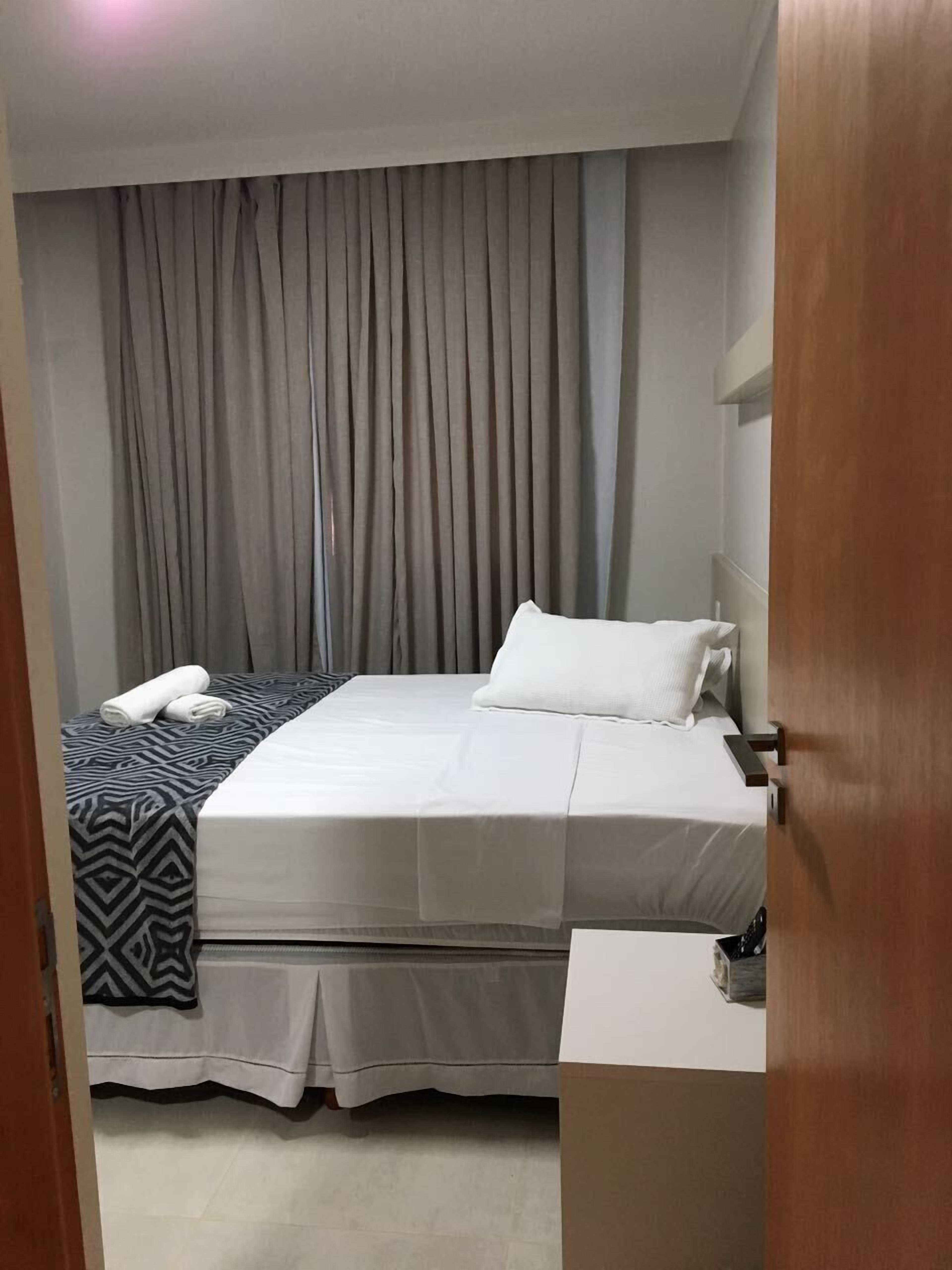 Una habitación de hotel con cama, mesita de noche, cortina y puerta.