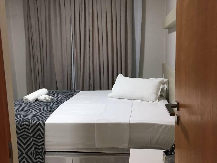 Una habitación de hotel con cama, mesita de noche, cortina y puerta.