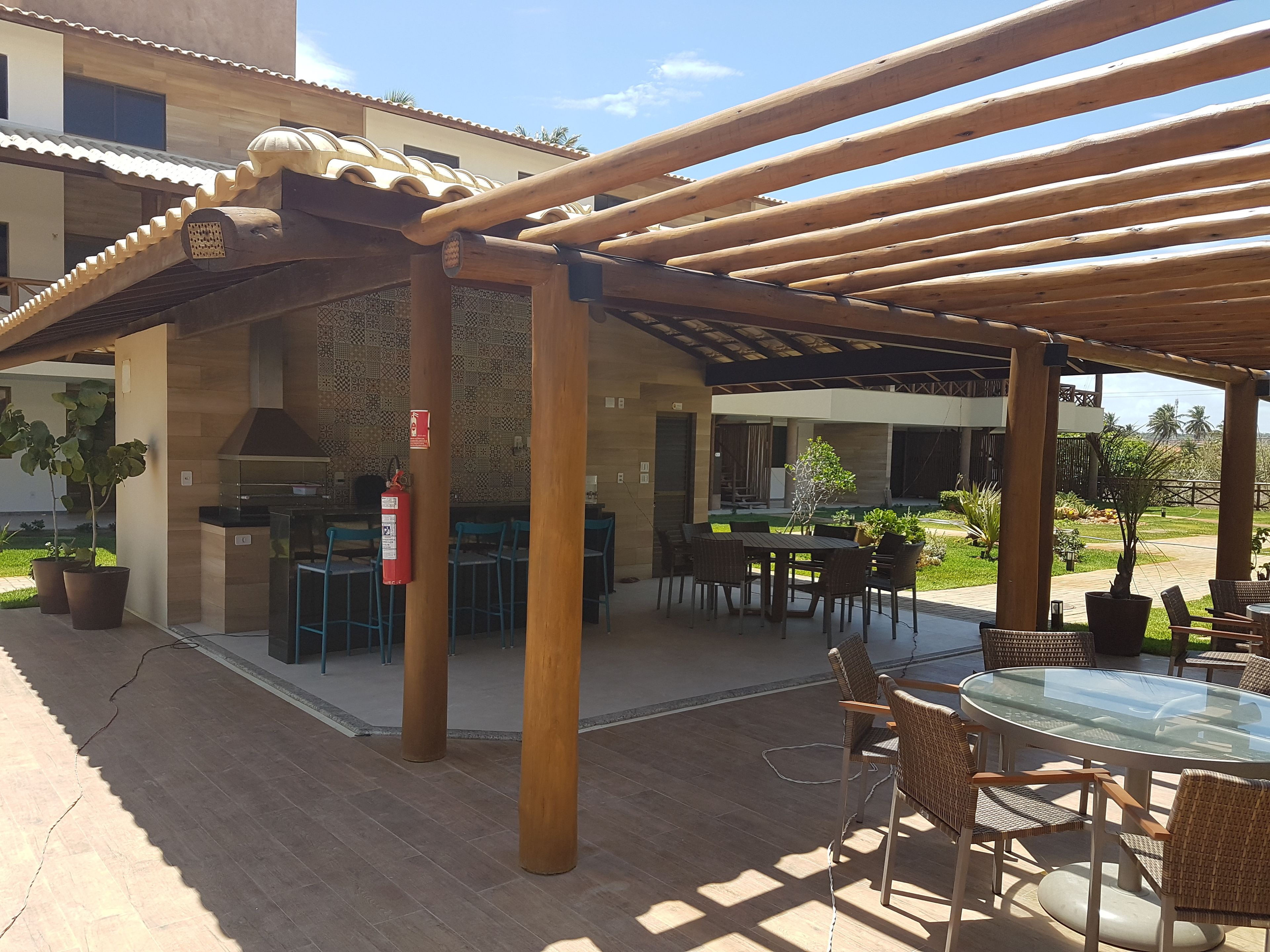 An outdoor patio with wooden pergola, tables, chairs, and potted plants.
