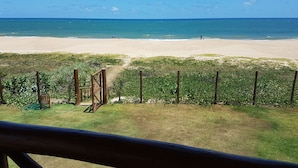 Vista de la playa con una valla de madera y una zona verde al frente.