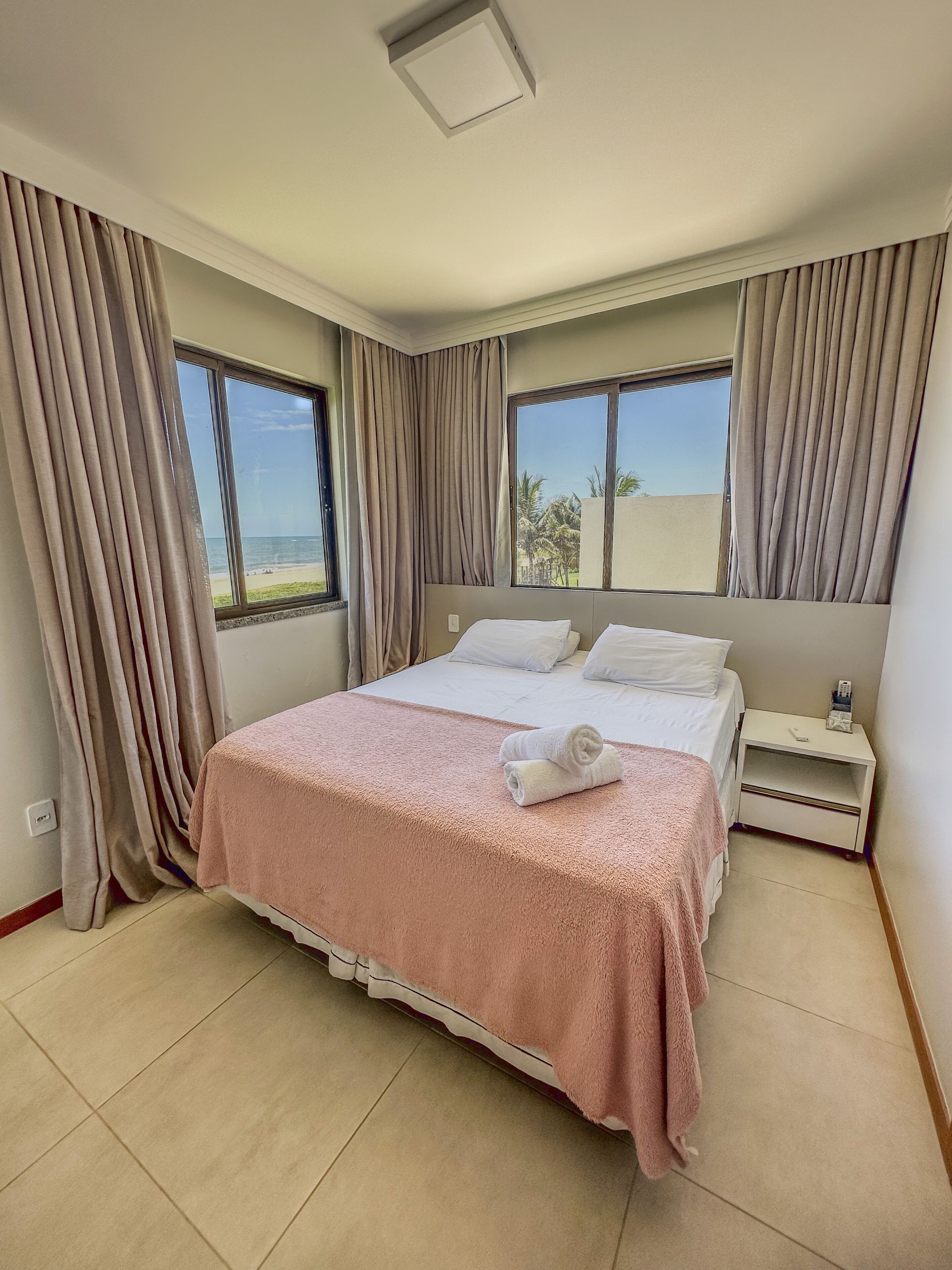 Una habitación de hotel con una cama grande, una mesita de noche y vistas a la playa.