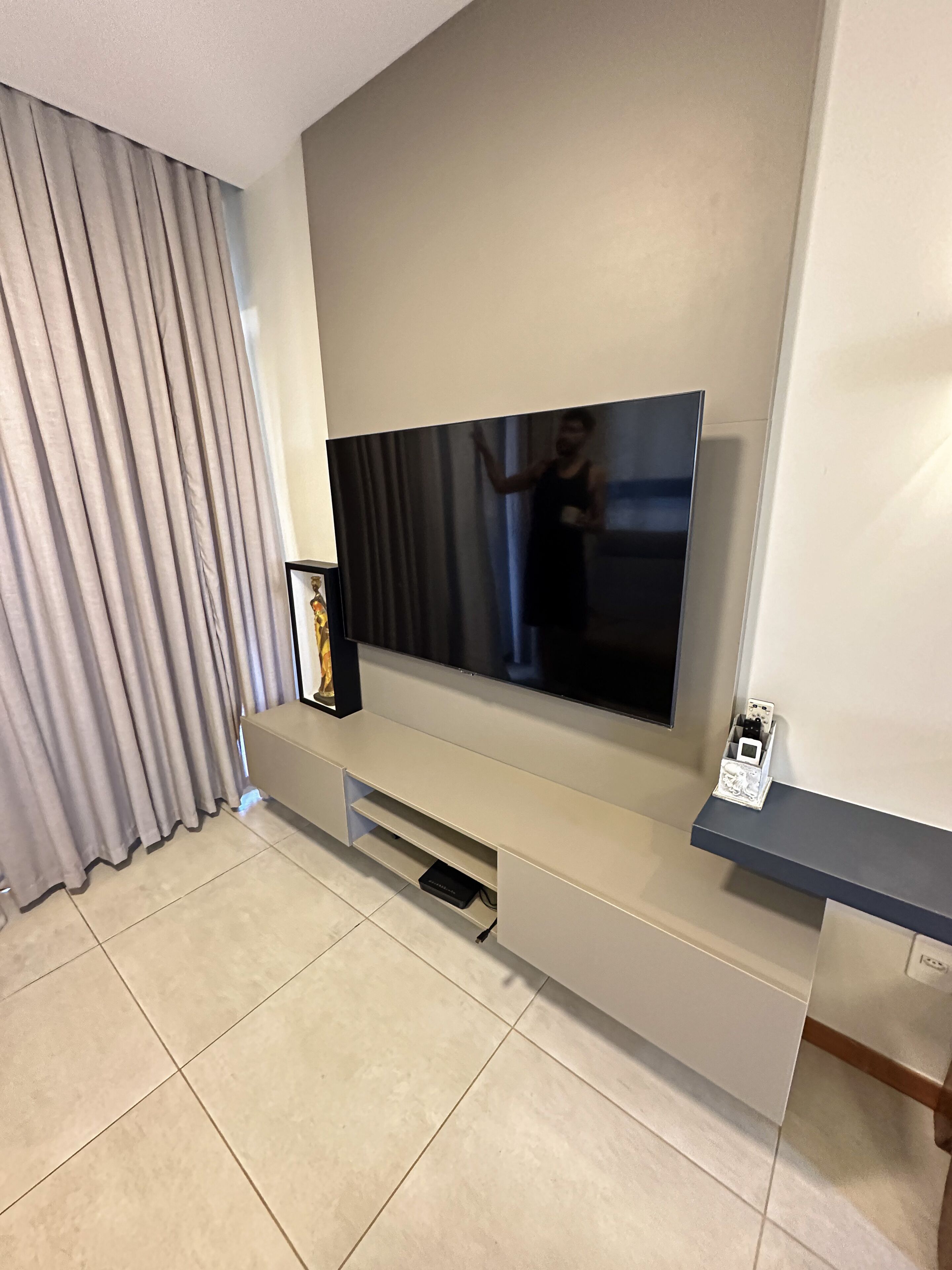 Uma sala de estar moderna com uma grande TV de tela plana na parede, um painel de entretenimento embutido abaixo e uma grande janela com cortinas.