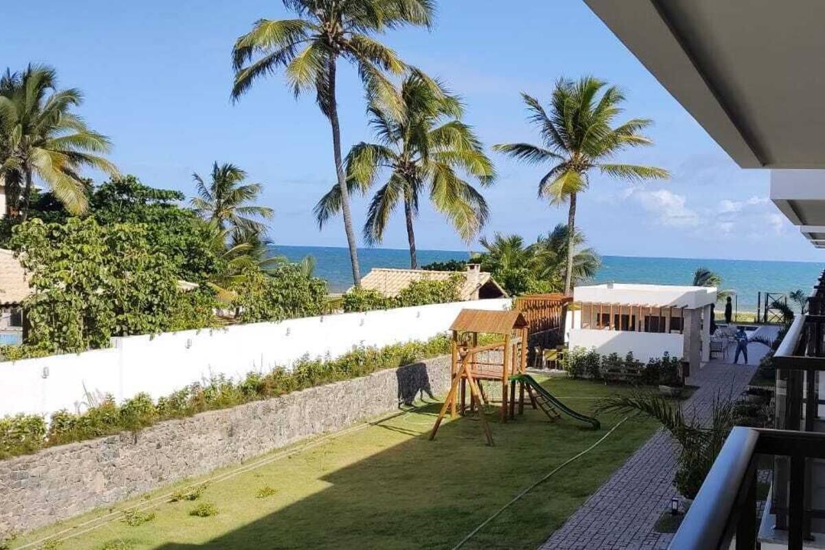 Un balcón con vista al océano, palmeras y una zona de juegos con un tobogán.