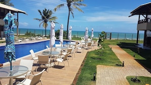 Zona junto a la piscina con sillones de descanso y sombrillas, vista despejada al océano y césped cuidado.