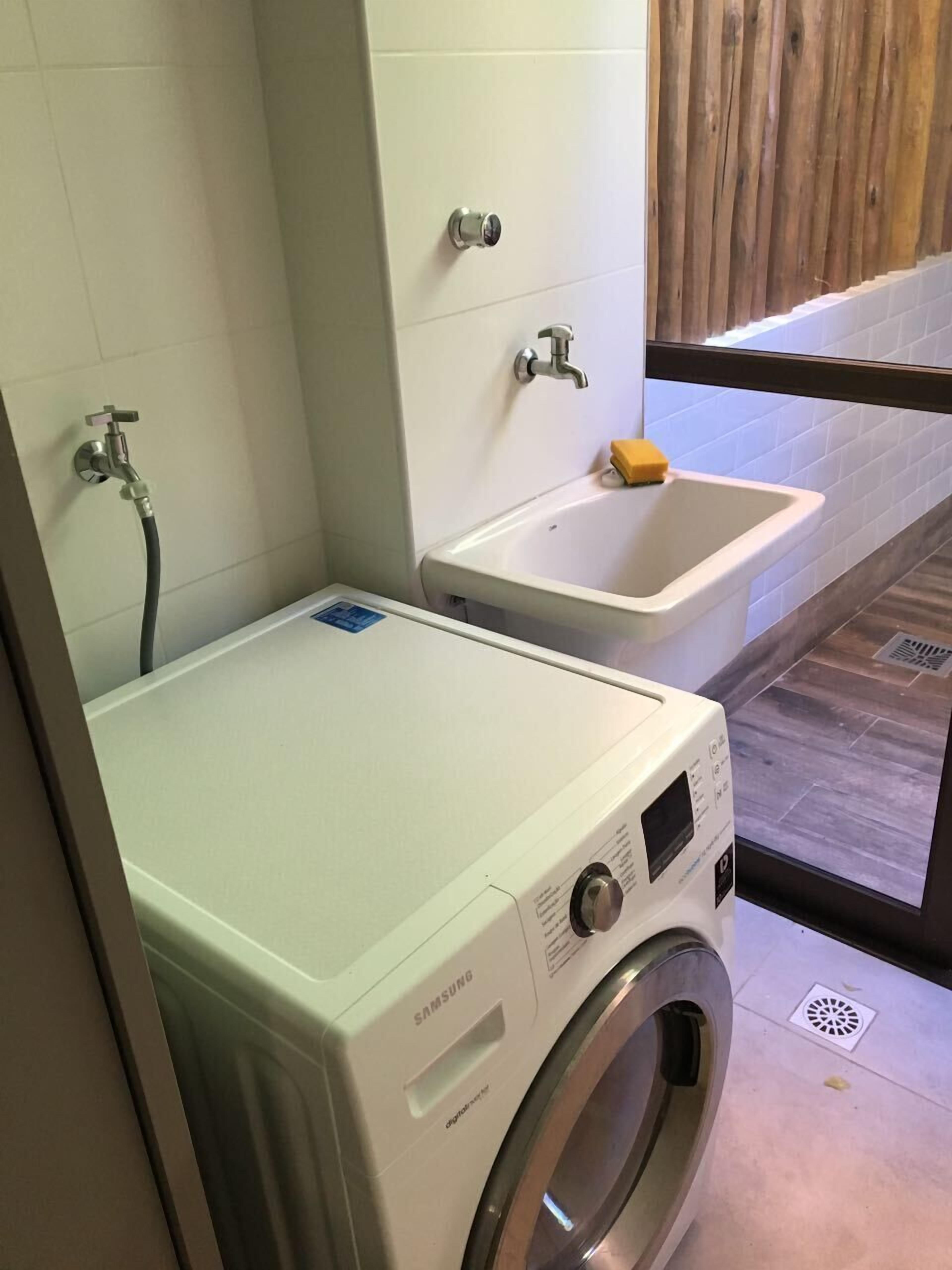 A Samsung washing machine in a bathroom with a sink and a wooden wall.
