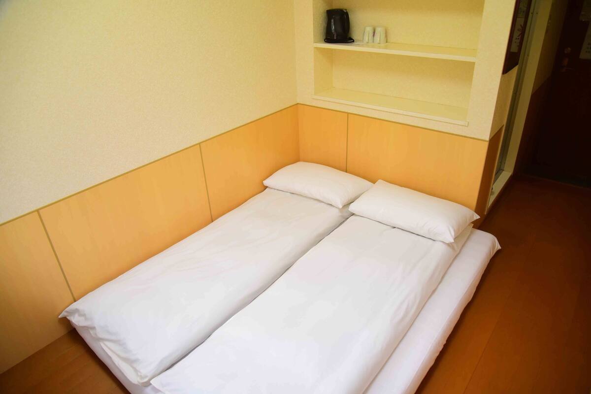 A single bed with white bedding in a room with wooden flooring and a beige wall.