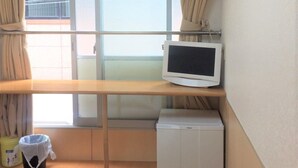 Una habitación de hotel con cama, un escritorio pequeño con monitor, un calentador y una ventana con cortinas.