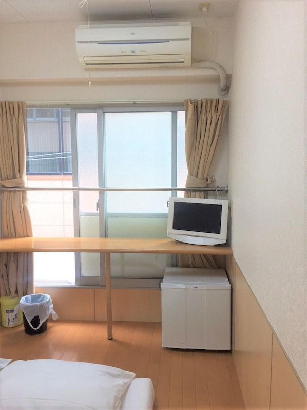 A hotel room with a bed, a small desk with a monitor, a heater, and a window with curtains.