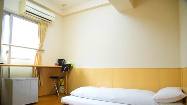 Una habitación pequeña y limpia con cama, escritorio y aire acondicionado.