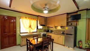 A compact kitchen with a dining area, wooden cabinets, a microwave, a refrigerator, and a ceiling fan. - TSL Unit H Well furnished Apartment (Cebu)
