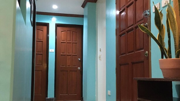 A hallway with two wooden doors, a potted plant, and a shelf. - TSL Unit H Well furnished Apartment (Cebu)