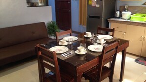 A dining area with a wooden table set for four, surrounded by chairs. A brown sofa is against the wall. - TSL Unit H Well furnished Apartment (Cebu)