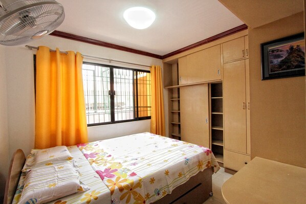A bedroom with a bed, a wardrobe, a window with curtains, and a ceiling fan.
