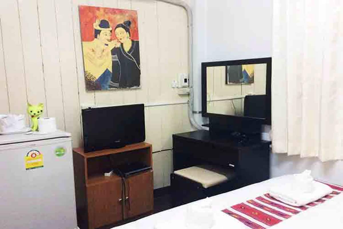 Een hotelkamer met een bed, een televisie, een klein kastje, een spiegel en een schilderij aan de muur.