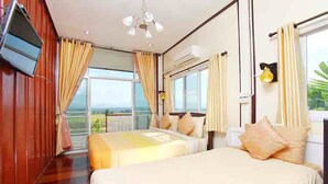 Habitación de hotel con dos camas, televisor y un ventanal grande con cortinas.
