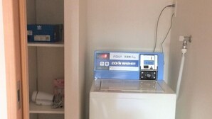 A compact, white, portable CO/N WASHER in a narrow hallway with a white wall and a wooden door frame. - uenohouse annex (Tokyo)