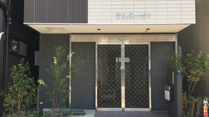 A building entrance with a modern design, featuring a metal gate with a cross pattern, a sign above the entrance, and some greenery around the base. - uenohouse annex (Tokyo)