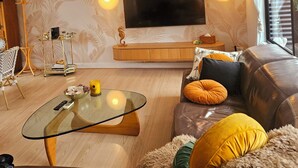 A modern living room with a leather sofa, glass coffee table, and a flat-screen TV mounted on the wall.