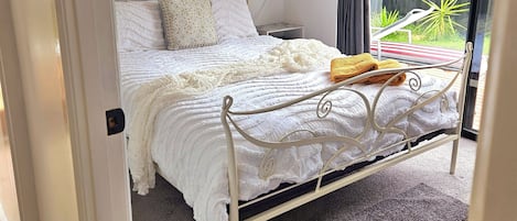 Een slaapkamer met een bed, gordijnen, een nachtkastje en uitzicht op het omliggende landschap.