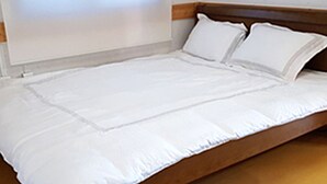 Ein ordentlich bezogenes Bett mit weißen Leinentüchern und einem Holzkopfende.