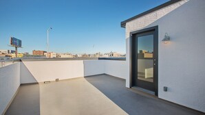 Eine Dachterrasse mit Glastür, weißen Wänden und freiem Blick auf die Stadtlandschaft.