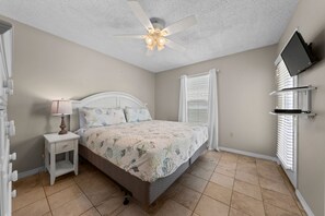 A bedroom with a bed, a nightstand, a ceiling fan, a window with blinds, and a mounted TV. - Sundial G3- The Beach is Where You Need to Be! (Gulf Shores)