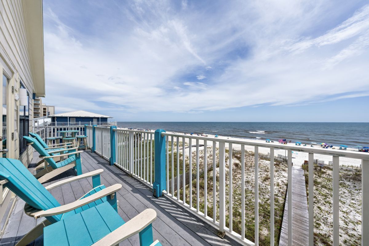 A deck with blue chairs overlooking a beach with a wooden walkway.