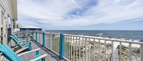 A deck with blue chairs overlooking a beach with a wooden walkway.