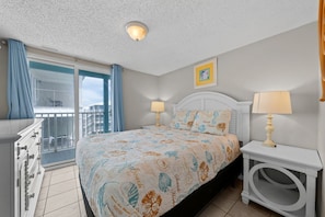 A bedroom with a bed, two bedside lamps, a window with curtains, a balcony, and a small wall-mounted picture.