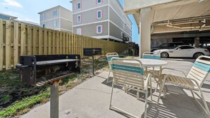 A patio area with a barbecue grill, outdoor seating, and a view of a multi-story building. - Sundial G3- The Beach is Where You Need to Be! (Gulf Shores)