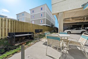 A patio area with a barbecue grill, outdoor seating, and a view of a multi-story building. - Sundial G3- The Beach is Where You Need to Be! (Gulf Shores)