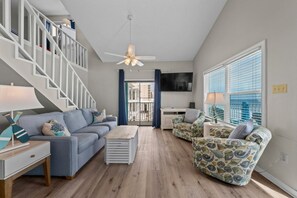 Un salon avec un escalier, un ventilateur de plafond, un téléviseur et une vue par la fenêtre.
