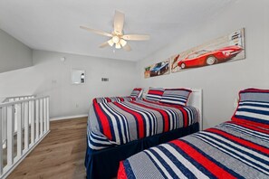 Une chambre avec deux lits, un ventilateur de plafond et un mur orné d’une affiche représentant une voiture et un hôtel.