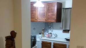 Un pasillo estrecho que conduce a una cocina con armarios de madera, un fregadero y una zona de comedor con una mesa y sillas.