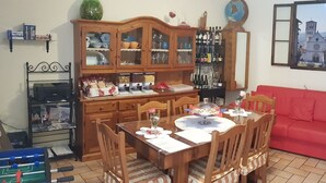 Una sala de estar acogedora con una mesa de comedor de madera, un sofá rojo y una estantería llena de libros y objetos decorativos.