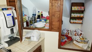 Una kitchenette con una cafetera, un espejo y diversos alimentos en estantes.